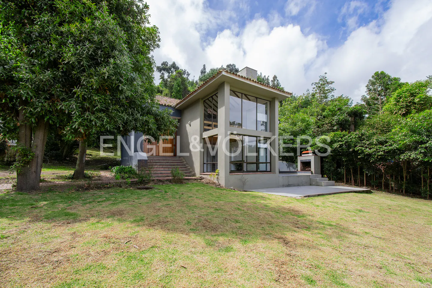 Exterior view of a modern two-story house with large windows, a lawn, and surrounding trees.