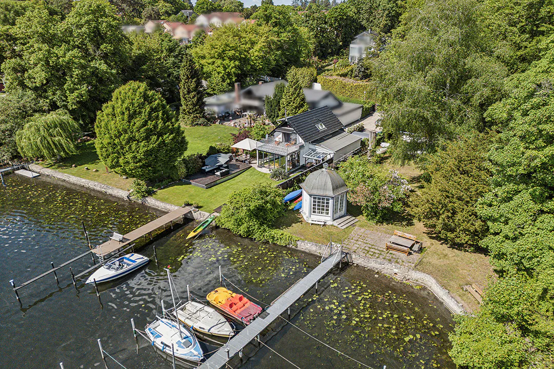Aerial view of a lakefront property with a house, gazebo, docks, and boats. Lush green trees surround the property.