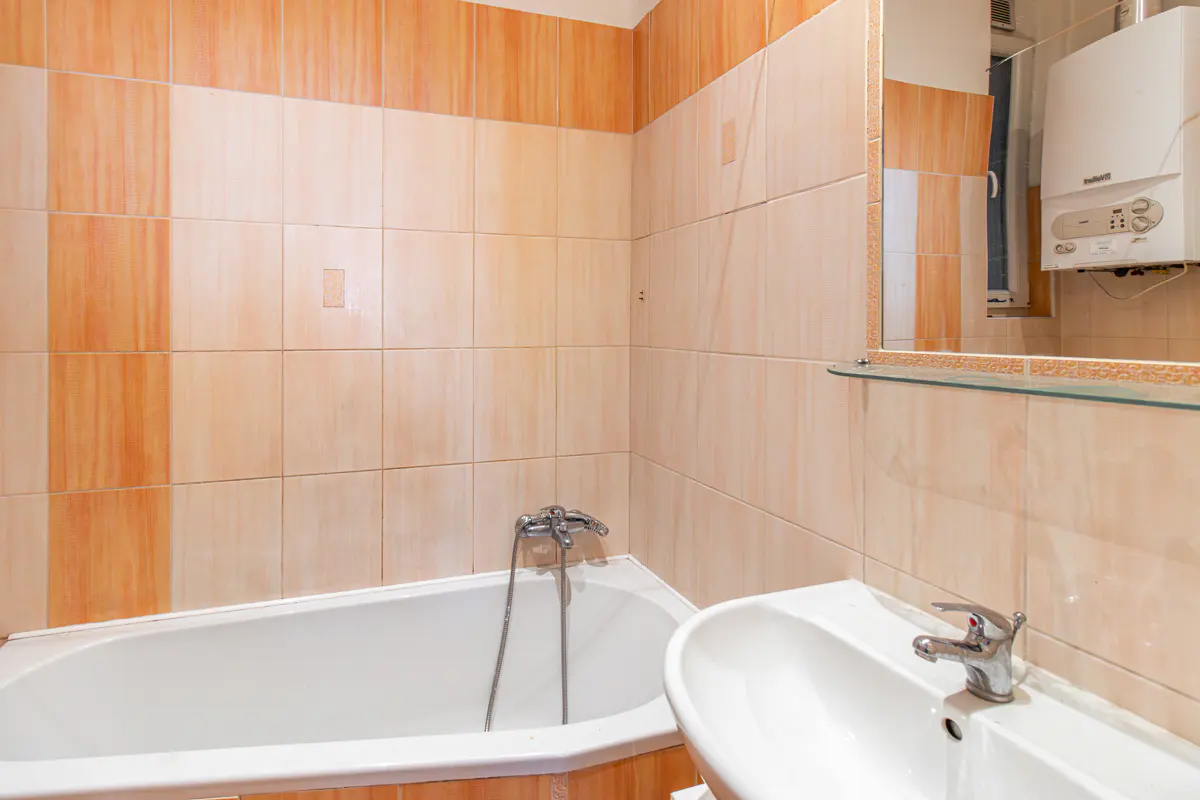 Bathroom with white tub, sink, and orange tile walls. A mirror reflects a water heater.