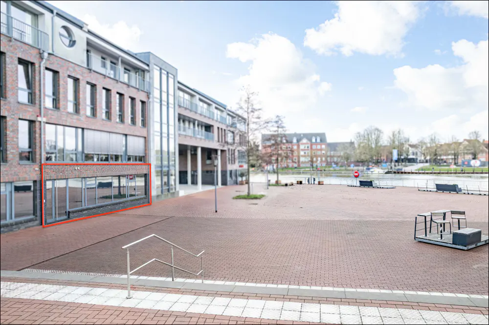 Exterior of a brick building with large windows, a brick plaza, and a waterfront view.