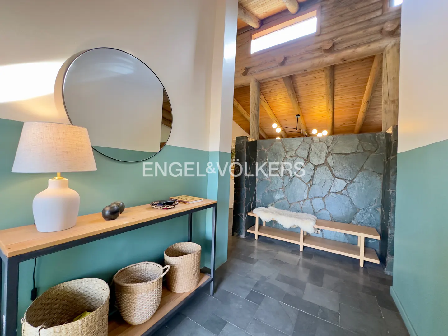 Entryway with a console table, round mirror, and a stone wall bench under a vaulted wood-beam ceiling.