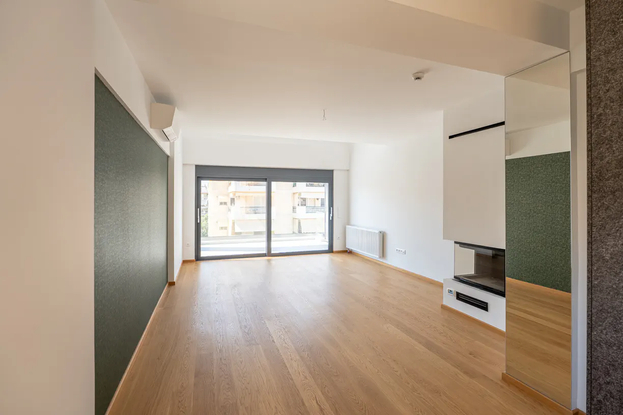 Bright, empty living room with wood floors, white walls, and a sliding glass door to a balcony. A modern fireplace is on the right.