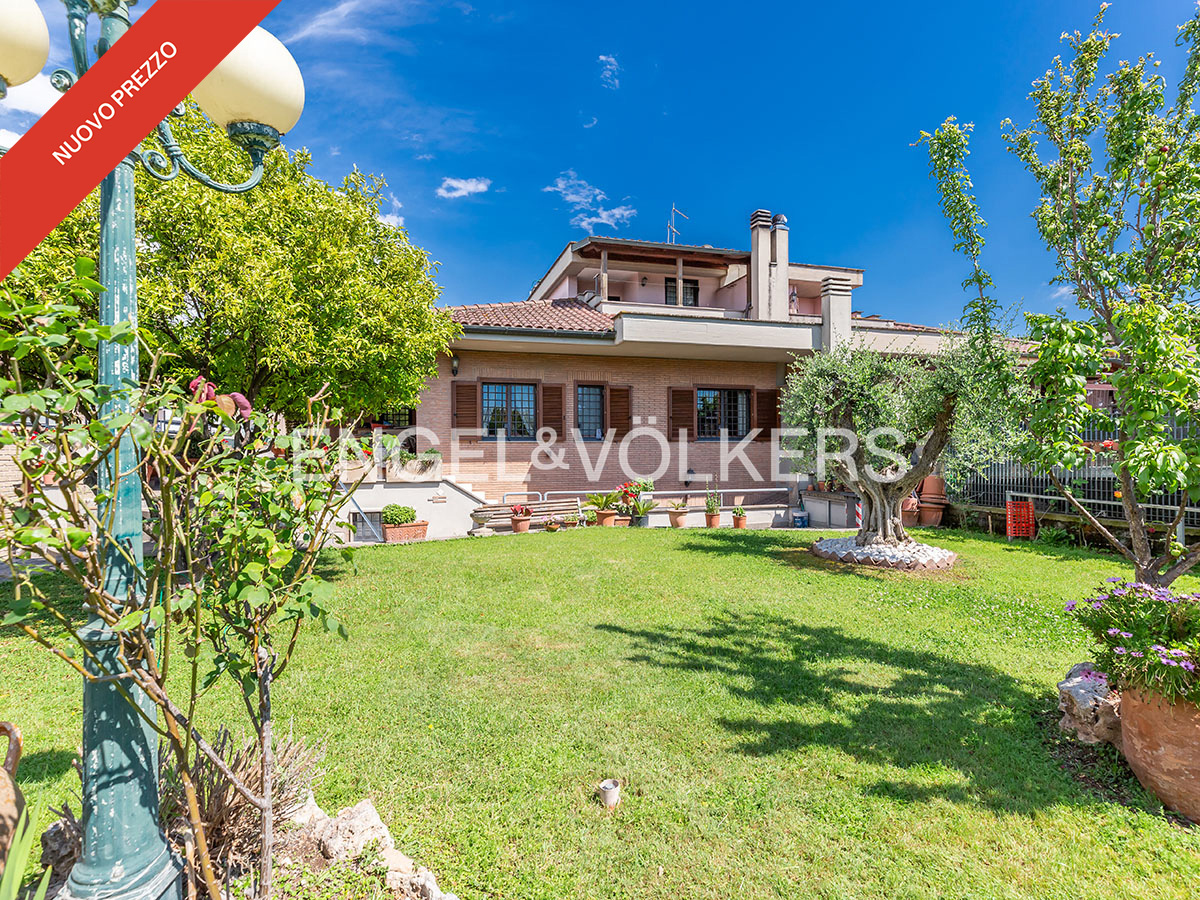 Two-story house with a green lawn, trees, and blue sky. A red banner in the upper left corner says "NUOVO PREZZO".