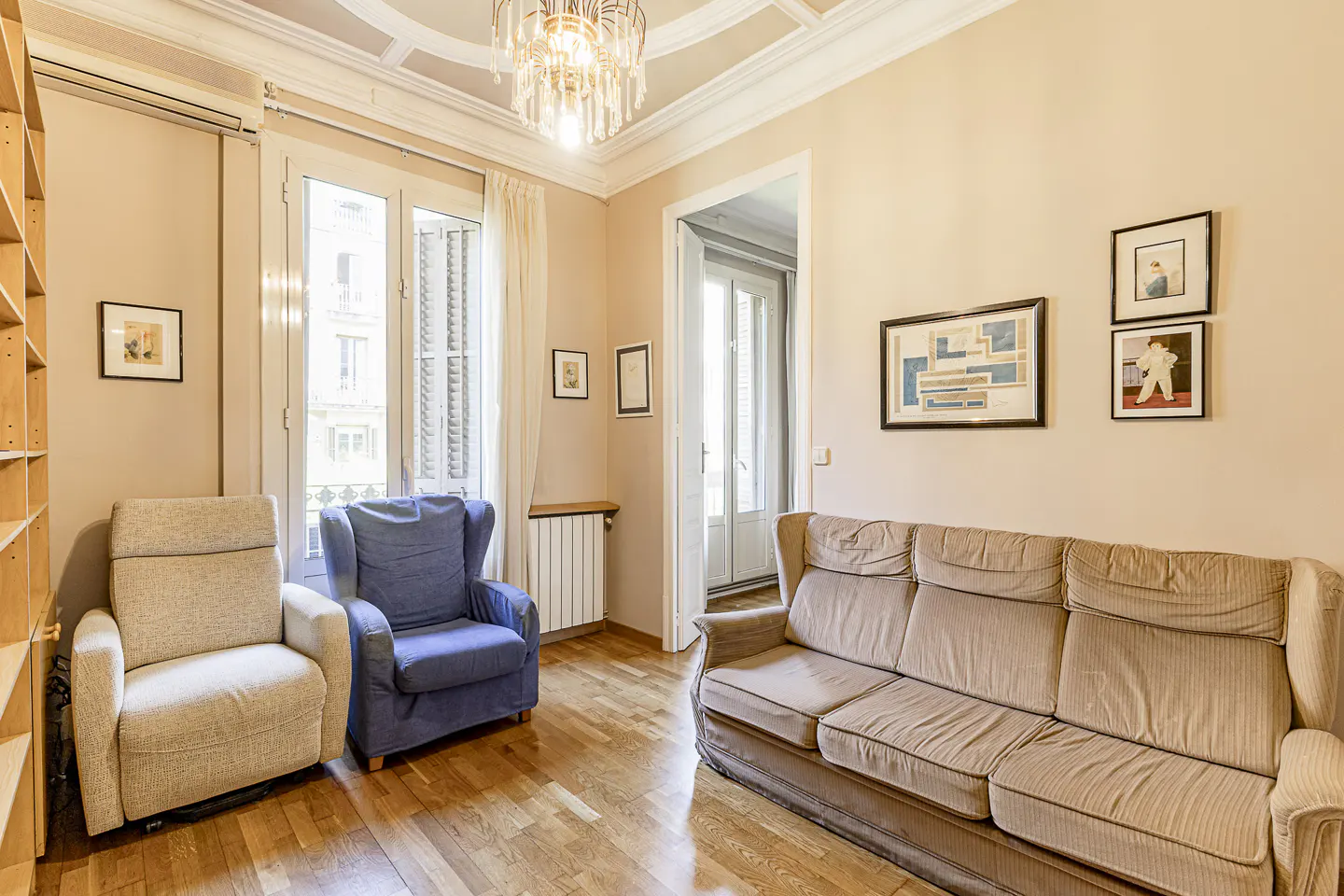 Living room with hardwood floors, beige walls, and a chandelier. There is a beige sofa, blue armchair, and a beige recliner.