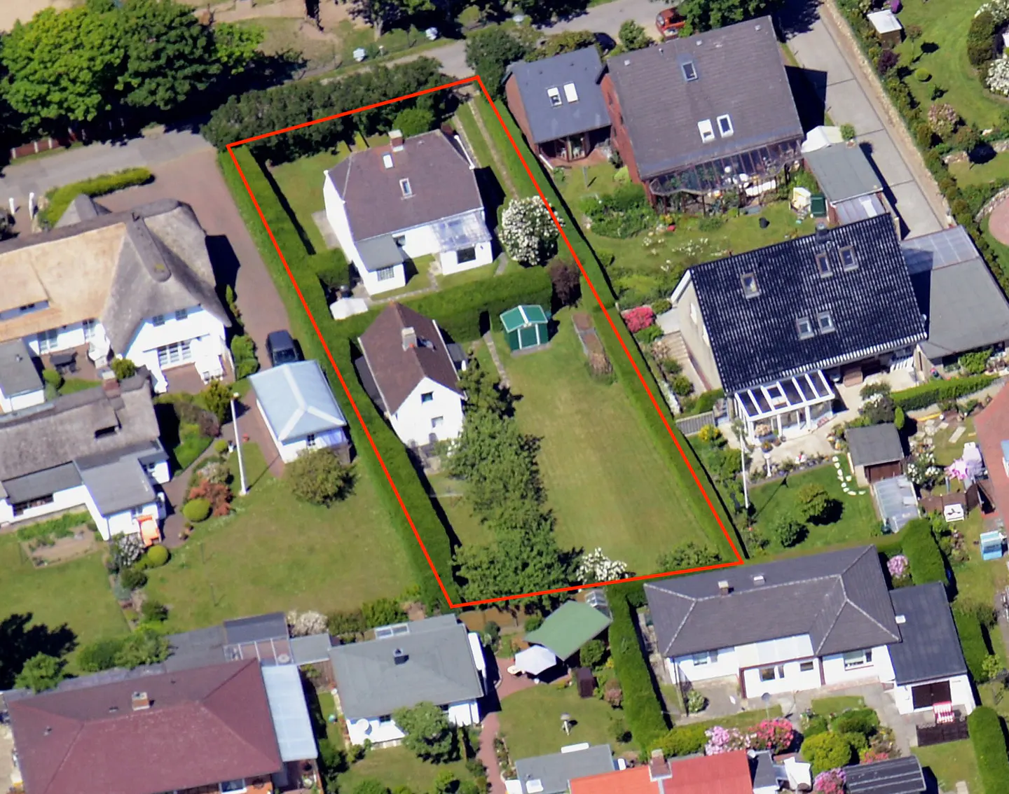Aerial view of a property outlined in red, featuring two white houses, a green lawn, and surrounding houses.