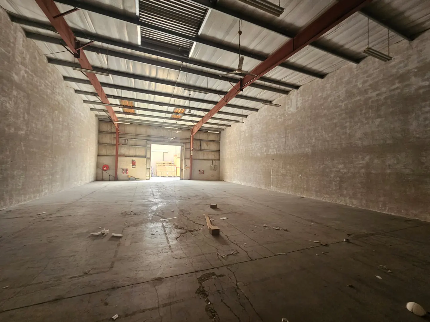 Empty warehouse interior with concrete floor and walls, metal ceiling beams, and open loading dock door at the back.