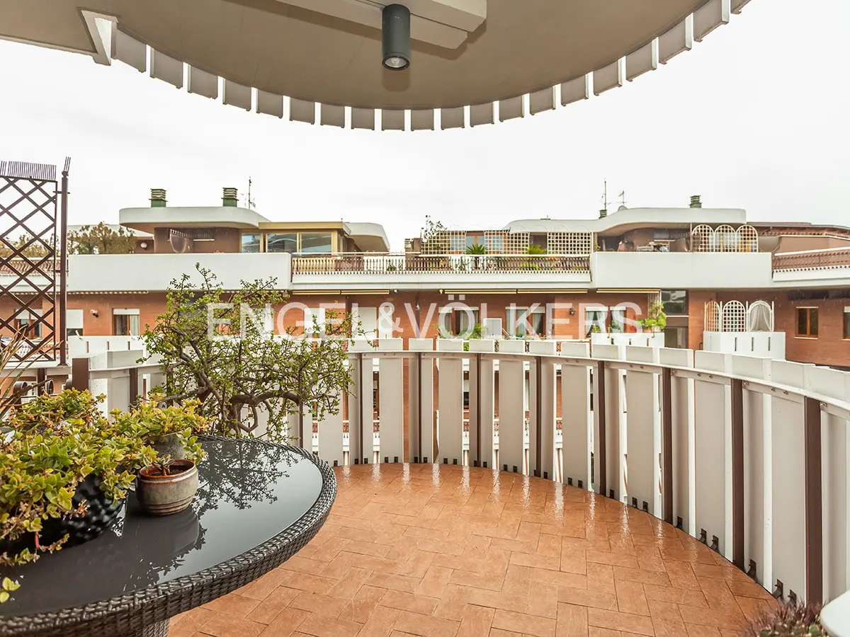 Balcony view with a round table, potted plants, and a white railing overlooking buildings. The Engel & Völkers logo is visible in the background.