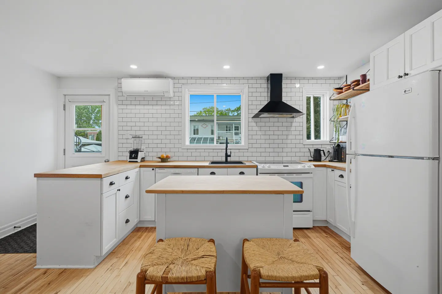 Bright, modern kitchen with white cabinets, butcher block countertops, and a central island with two woven stools.