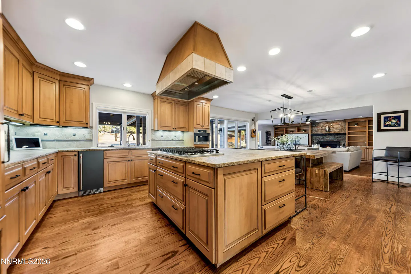 Open concept kitchen with wood cabinets, granite countertops, and a large island with a cooktop. Living room in background.