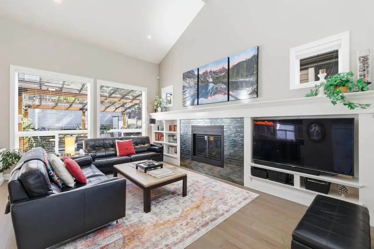 Living room with black leather sofas, a fireplace, and a large TV. A landscape painting hangs above the fireplace. Large windows let in natural light.