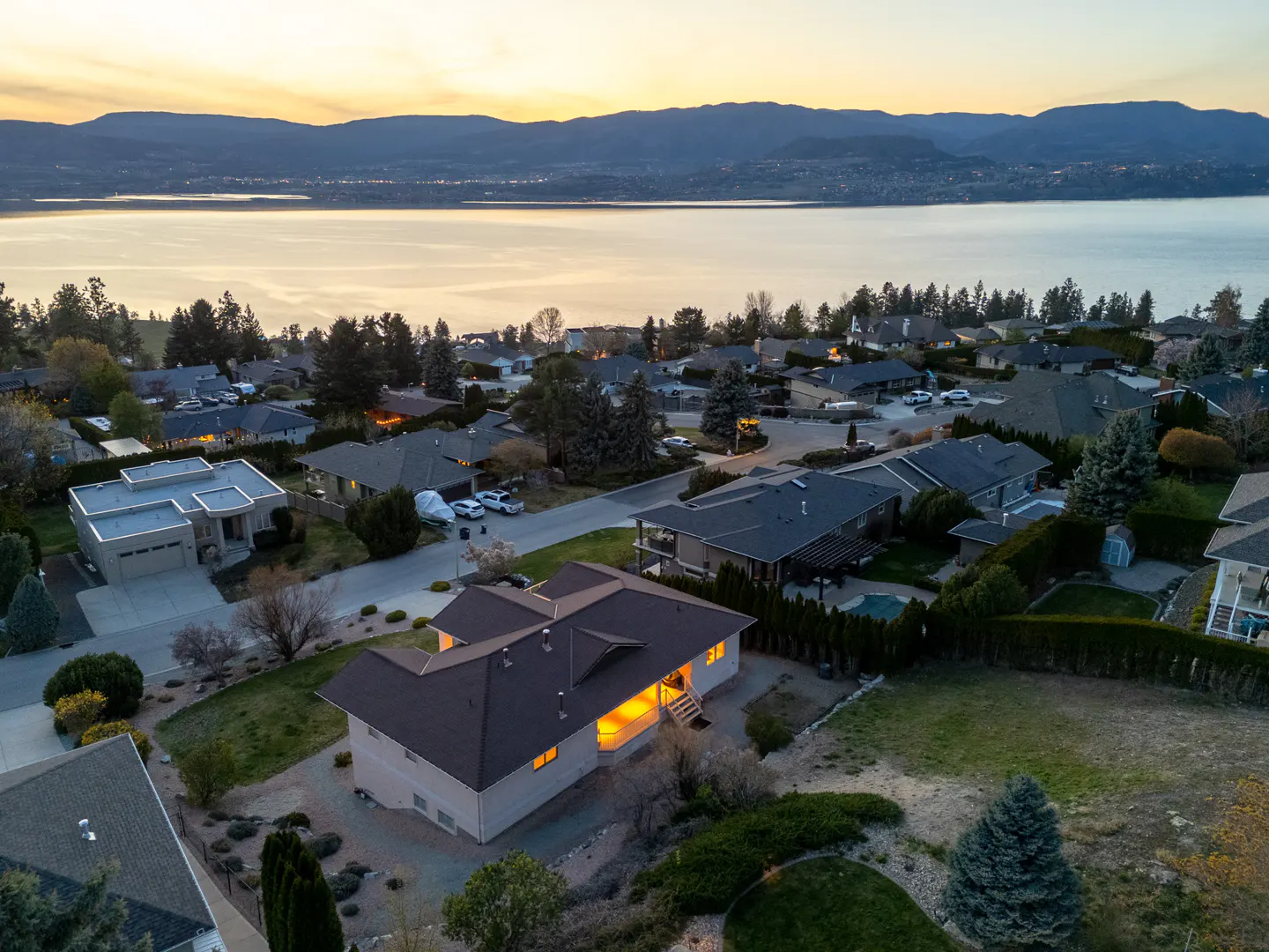 Aerial view of a residential neighborhood with houses, trees, and a lake in the background at sunset.