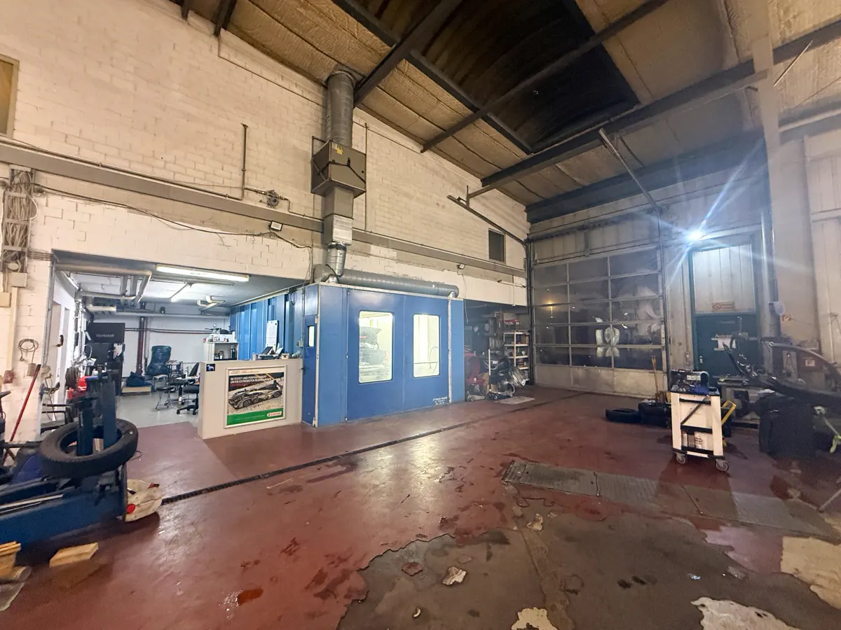 A wide shot of a large auto repair shop with a blue paint booth, tools, and a large garage door.