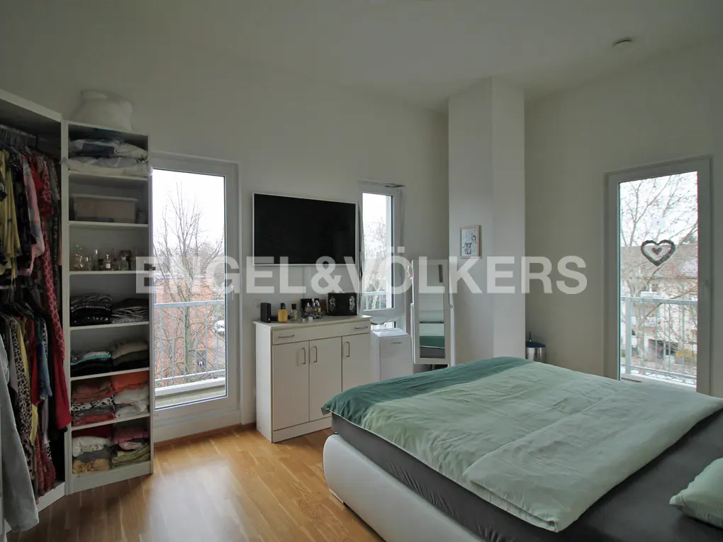 Modern bedroom with light wood floors, a bed with green bedding, a white wardrobe, and a TV mounted above a white cabinet.