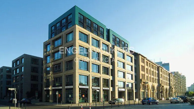 Modern commercial building with a teal top floor, beige facade, and large windows, street view.