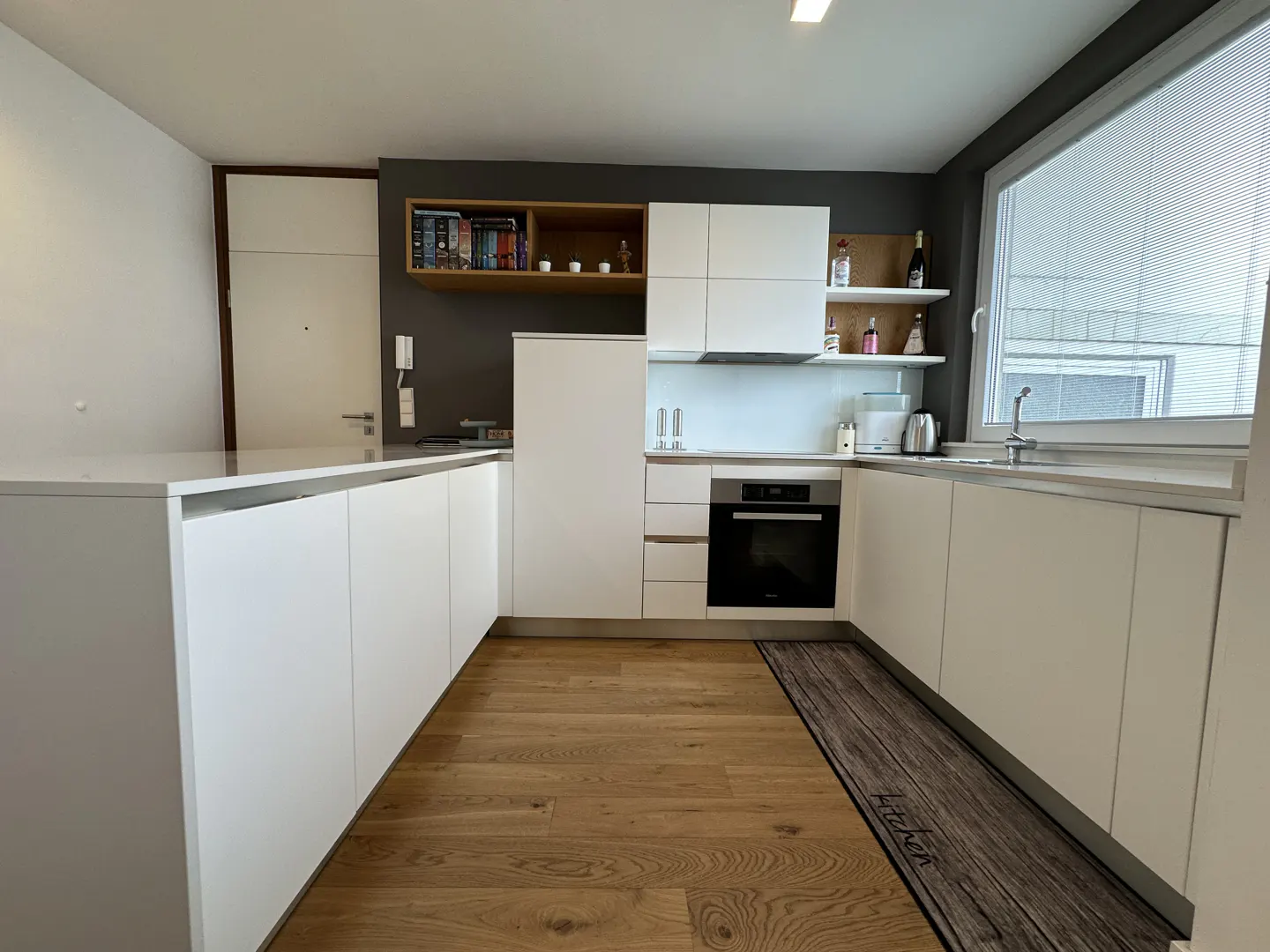 Bright kitchen with white cabinets, wood floors, and a gray accent wall. A large window provides natural light.