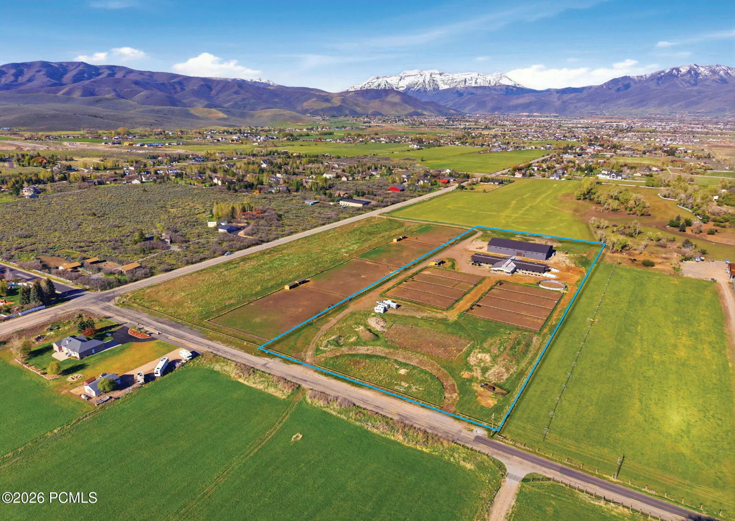 Aerial view of a large, fenced horse property with barns, fields, and mountain views in a rural setting.