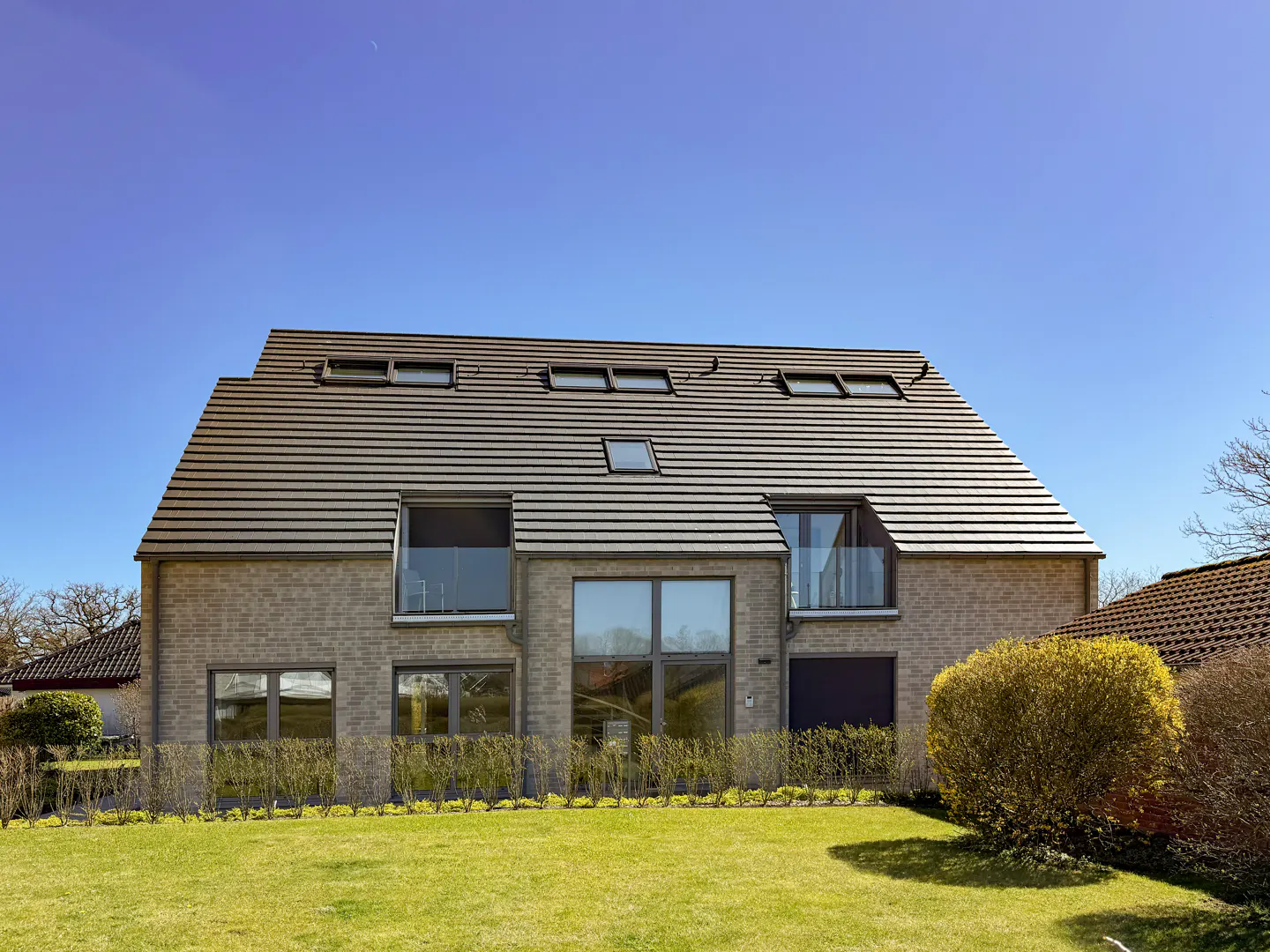 A two-story brick house with a gray tiled roof and green lawn under a clear blue sky.