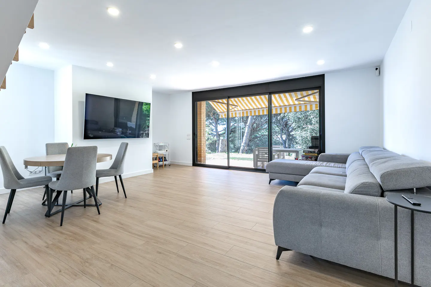 Bright, modern living room with a gray sectional sofa, round table with chairs, and a large sliding glass door to a patio.
