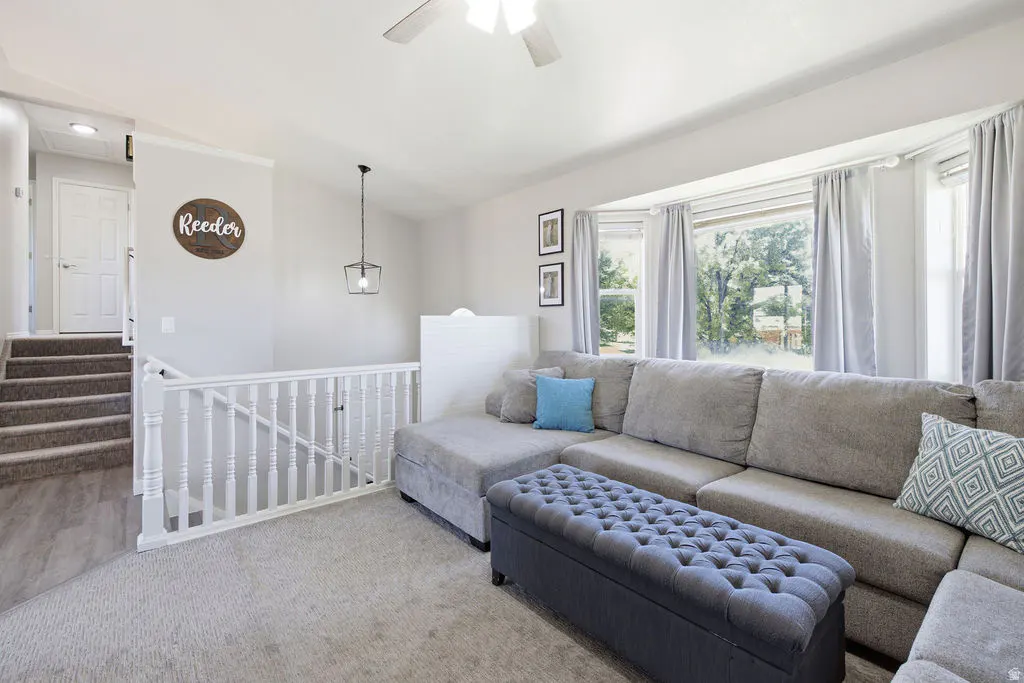 Bright living room with a large gray sectional, tufted ottoman, and stairs leading to a white door.