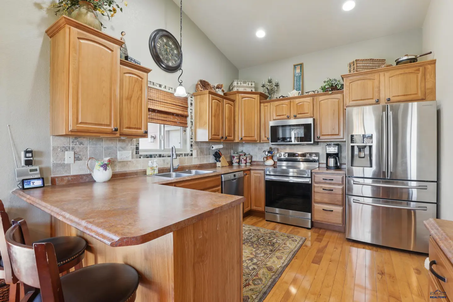 Kitchen with light wood cabinets, stainless steel appliances, brown countertops, and a breakfast bar with two stools.