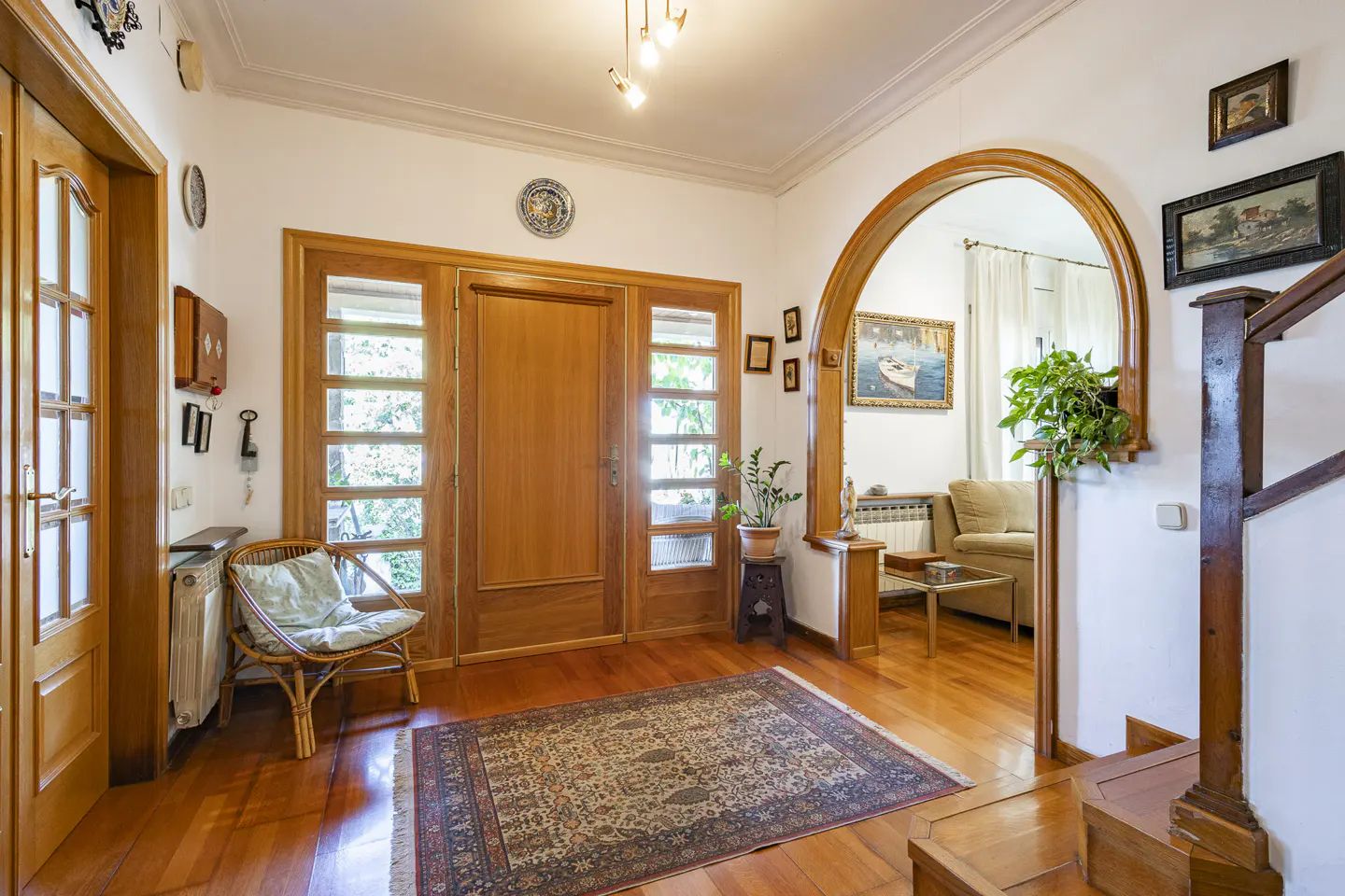Bright foyer with wood floors, a patterned rug, and a wooden front door with sidelights. An arched doorway leads to the living room.