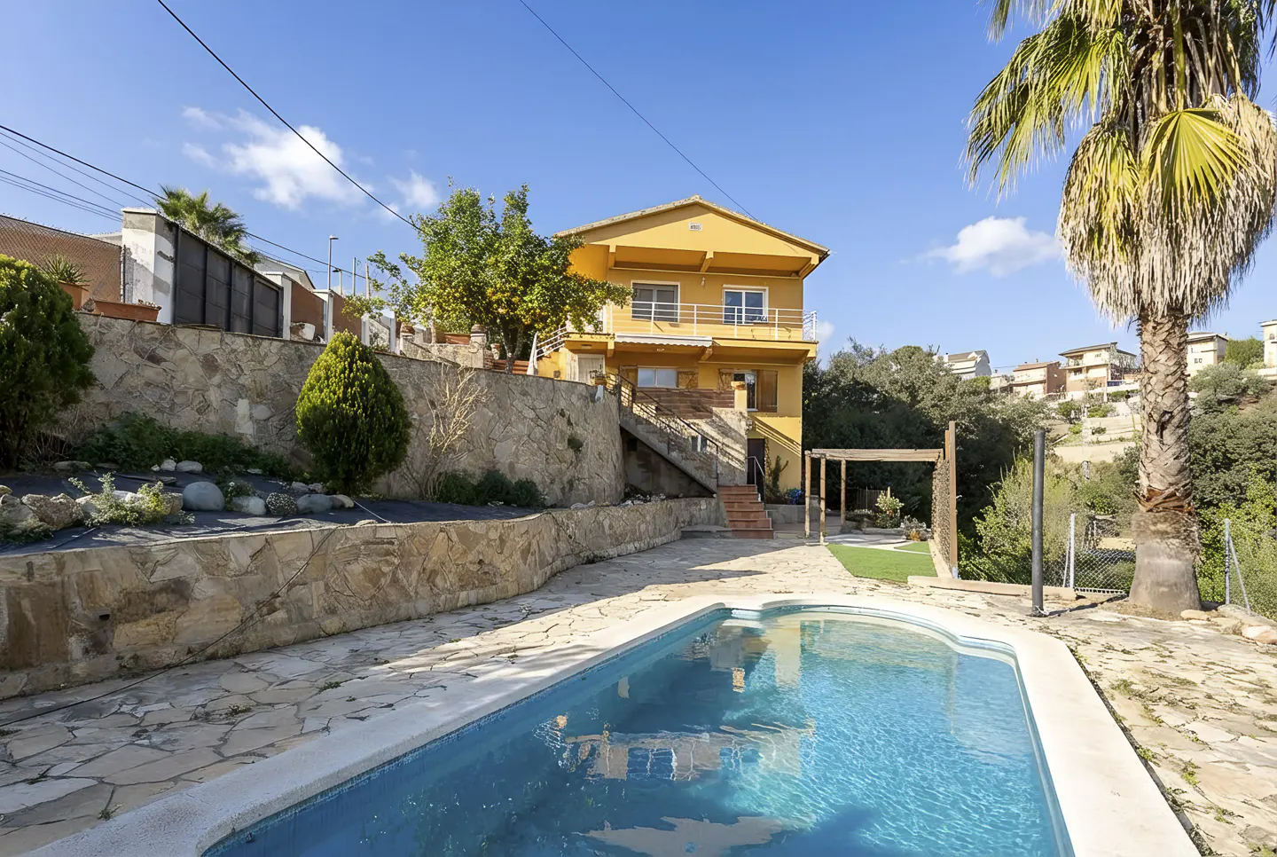 A yellow two-story house with a blue swimming pool in the foreground on a sunny day.