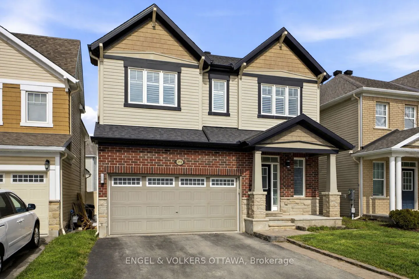 Two-story house with beige siding, brick accents, and a two-car garage on a sunny day.