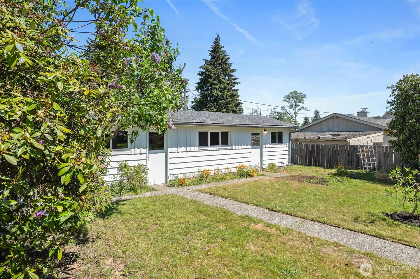 A white, one-story house with a gray roof, green lawn, and a concrete walkway on a sunny day.