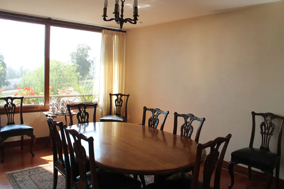 Dining room with an oval wood table surrounded by dark wood chairs. A window overlooks a green lawn and trees. A chandelier hangs above.