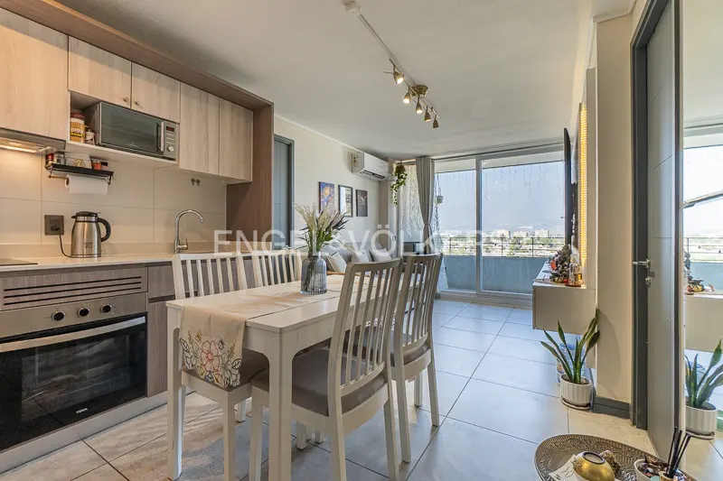 A bright apartment interior with a dining table, kitchen, and balcony overlooking a cityscape.