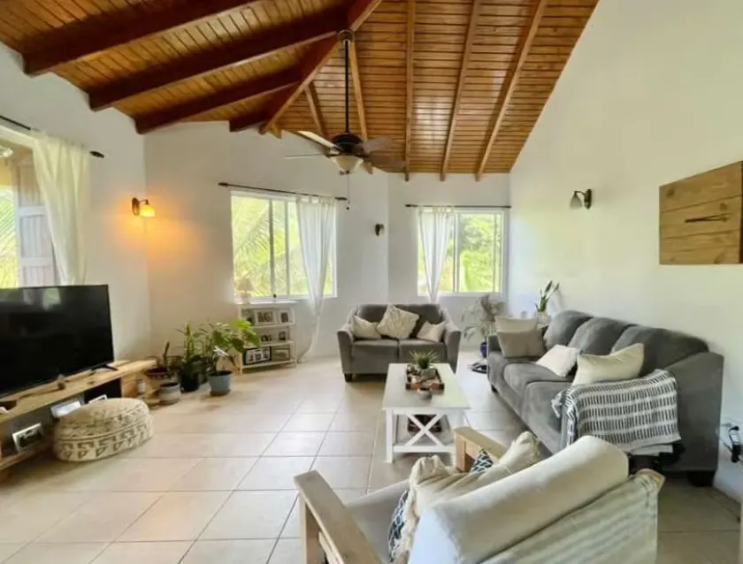 Bright living room with white walls, tile floors, and a wood-paneled ceiling. Gray sofas and a white coffee table furnish the space.