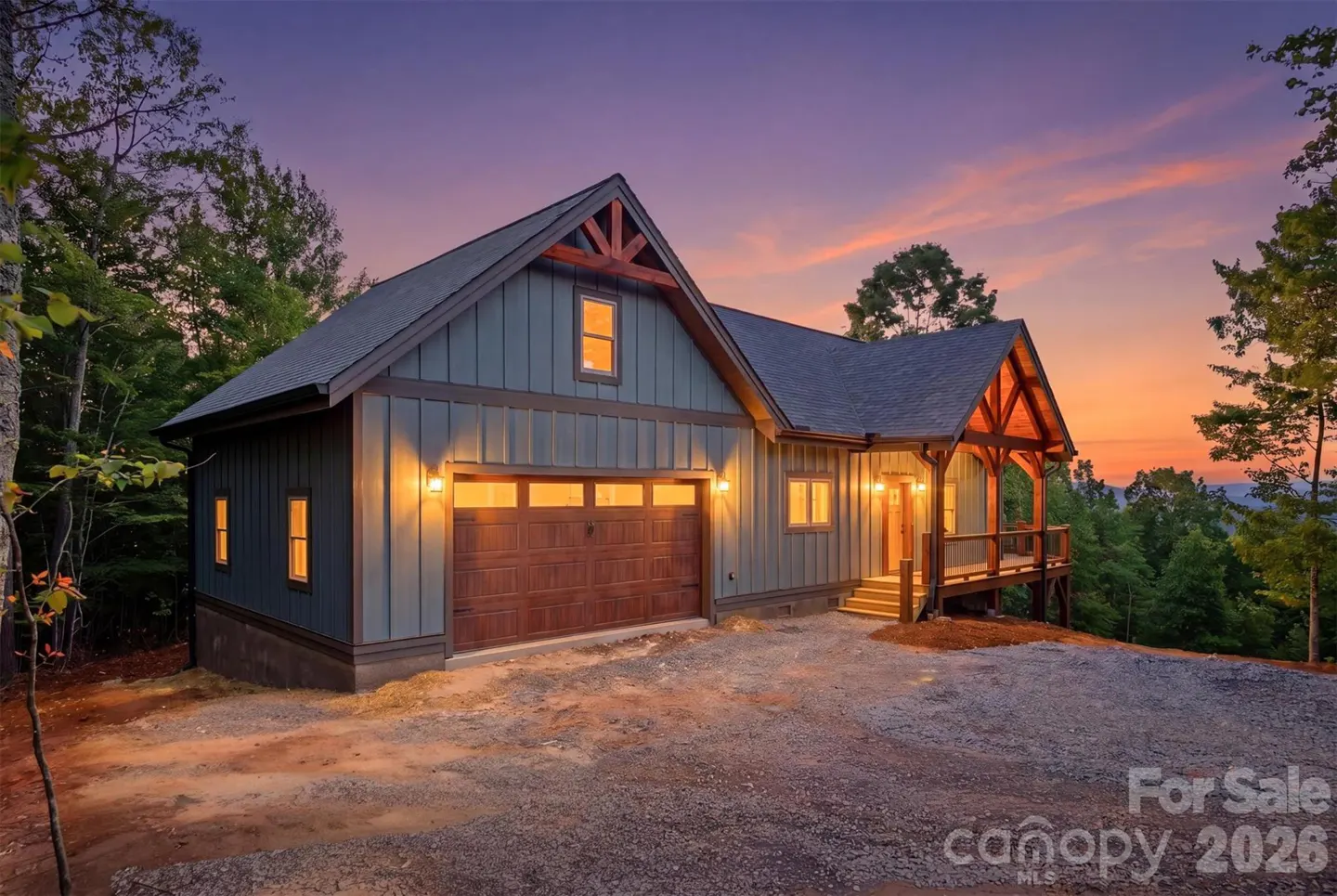 Exterior of a blue house with a brown garage door and porch at sunset.