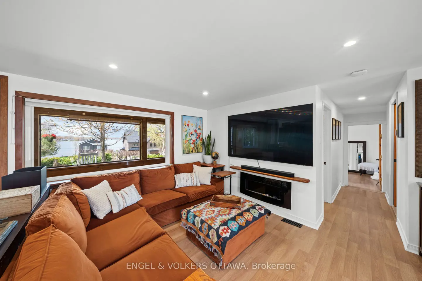 Living room with a large brown sectional sofa, a TV over a fireplace, and a window with a view of a lake.