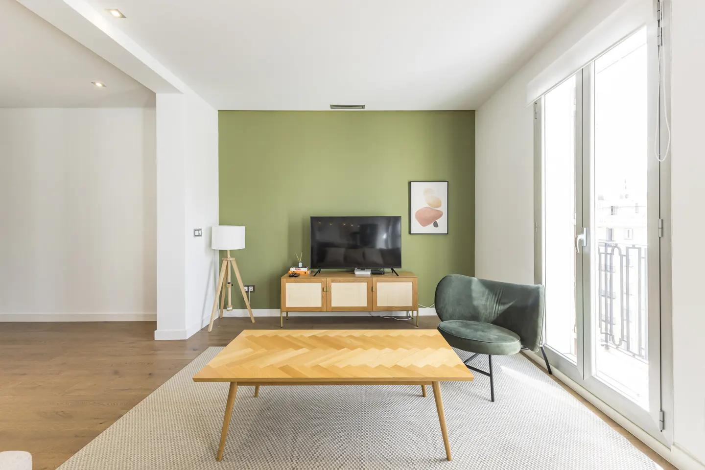 Bright living room with green accent wall, TV on cabinet, wood coffee table, green chair, and sliding glass doors.
