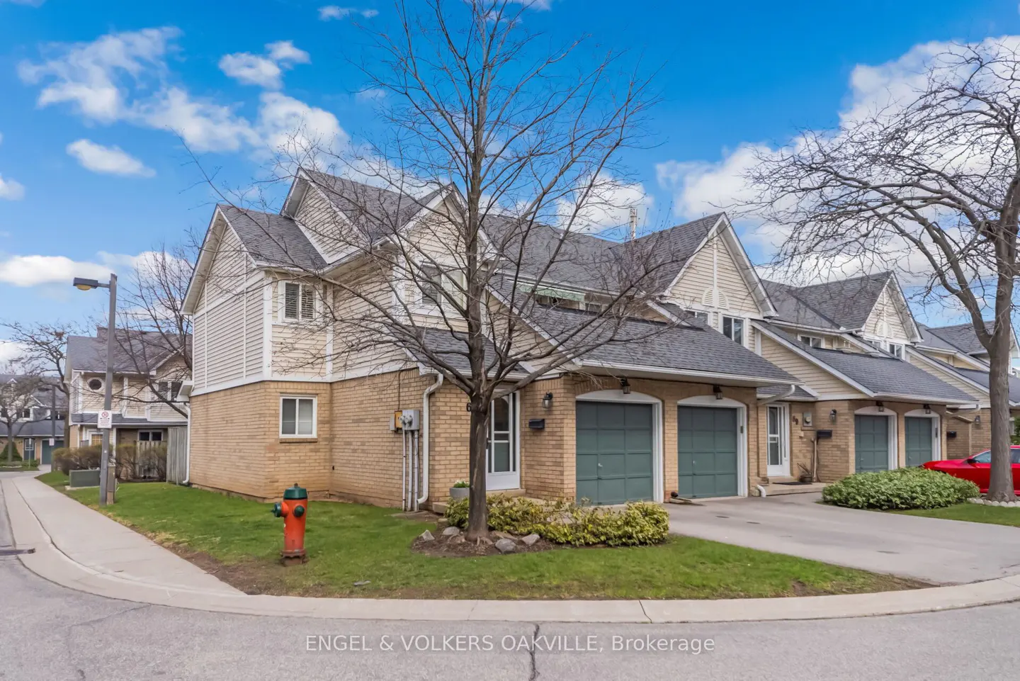 Row of townhouses with brick and siding exteriors, green garage doors, and a tree in the front yard. Blue sky with clouds.