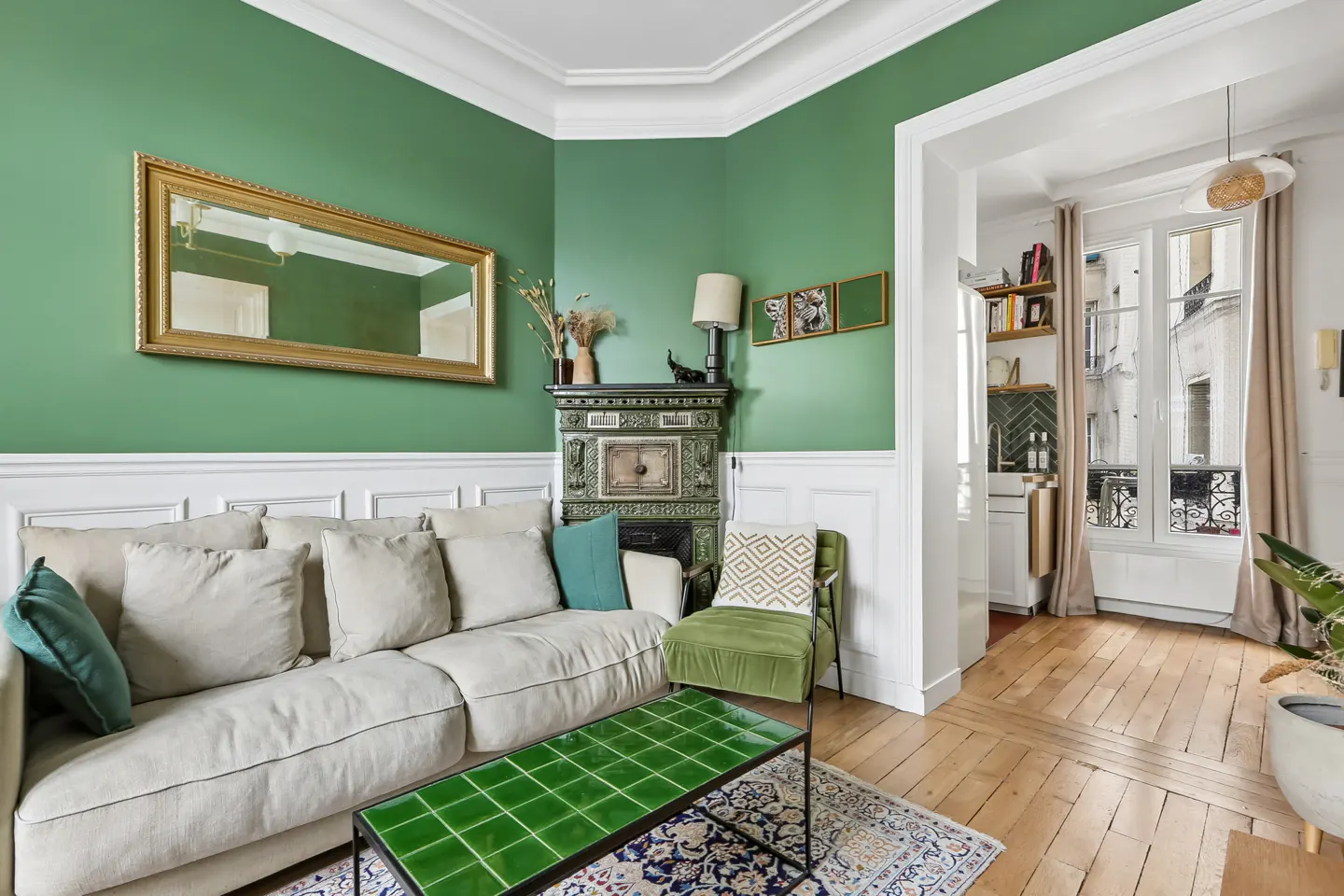 Living room with green walls, white sofa, green tiled coffee table, and a view into a bright kitchen.