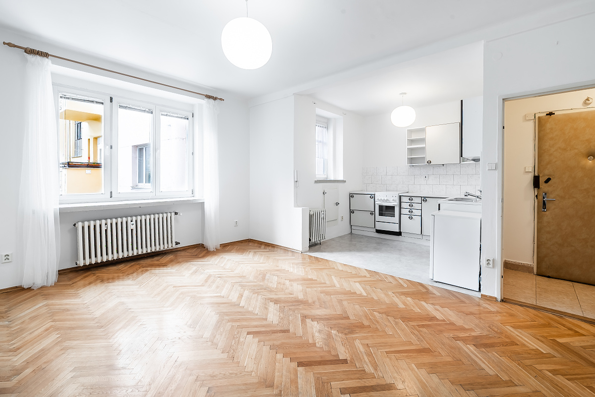 Bright, open-plan apartment with herringbone wood floors, white walls, a modern kitchen, and large windows with curtains. [AI-generated text]