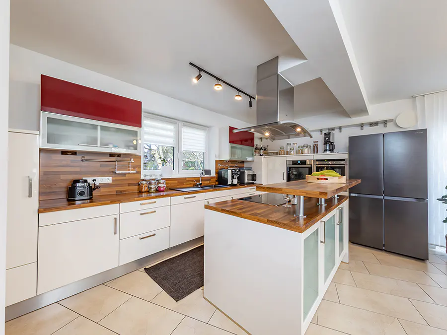 Bright kitchen with white cabinets, wood countertops, and stainless steel appliances. A kitchen island stands in the center.