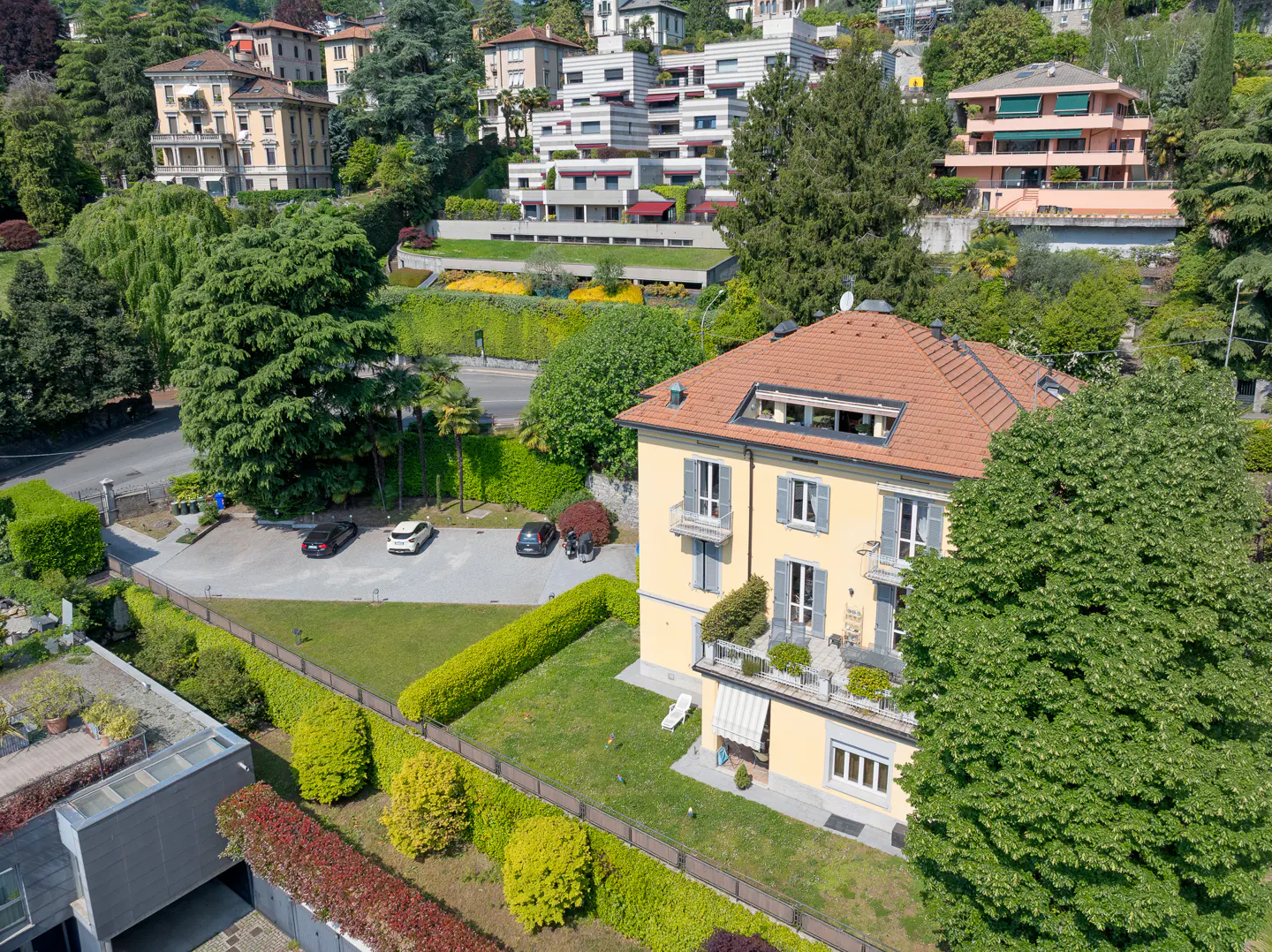 Aerial view of a yellow house with a red tile roof, blue shutters, and green landscaping.