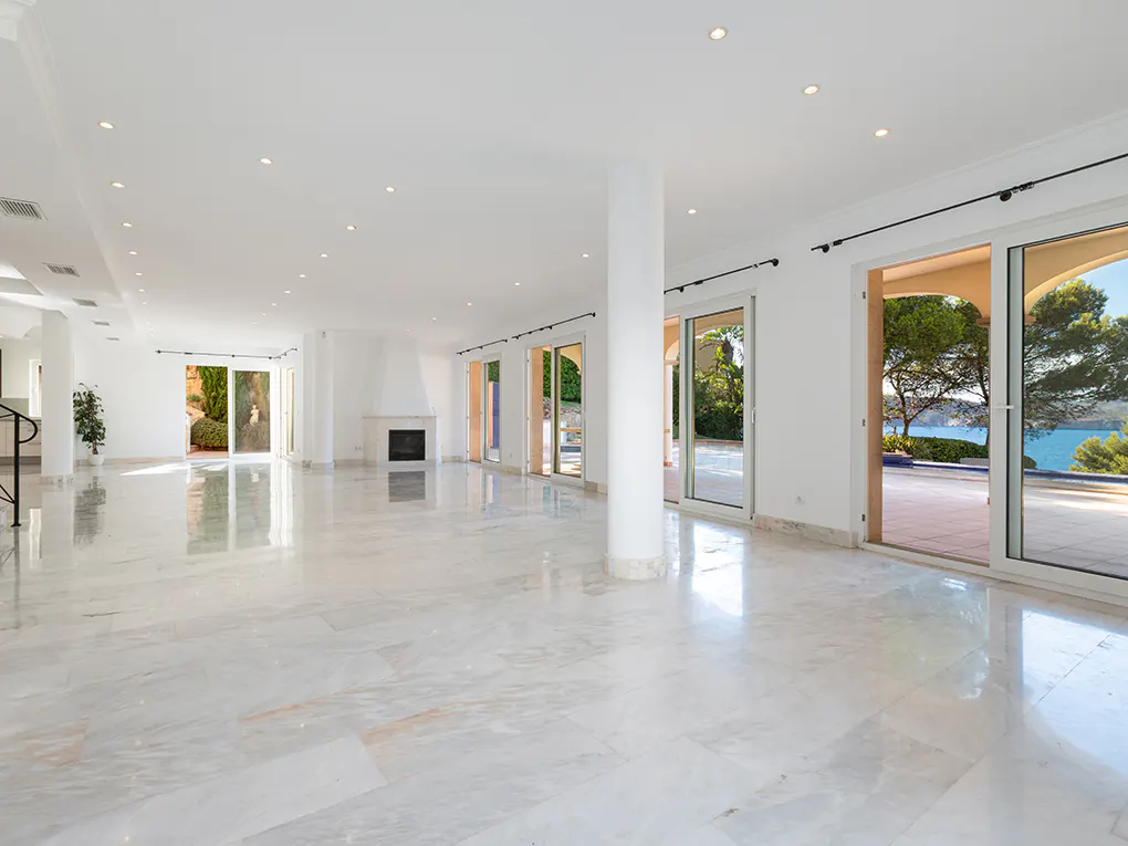 Bright, empty room with white walls, marble floors, and a fireplace. Sliding glass doors open to a patio with ocean views.