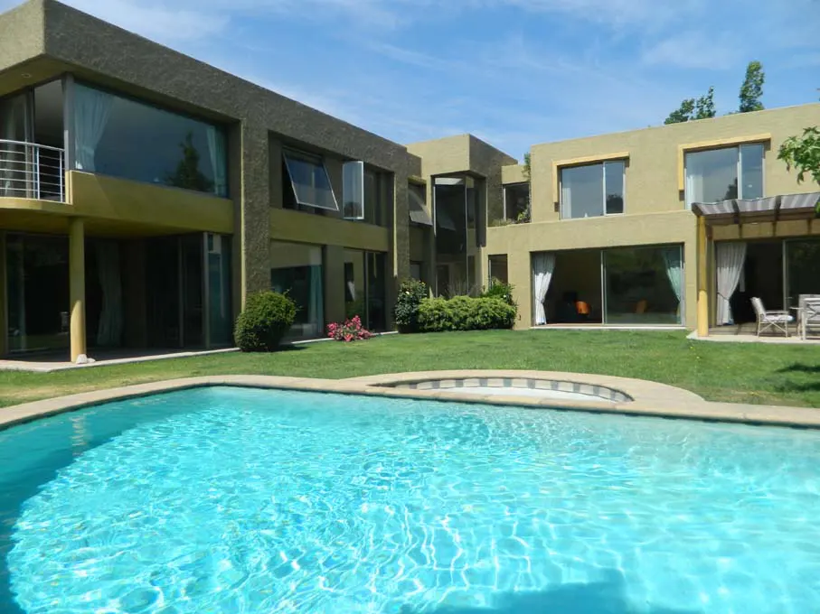 A modern, two-story house with a turquoise swimming pool and green lawn on a sunny day.