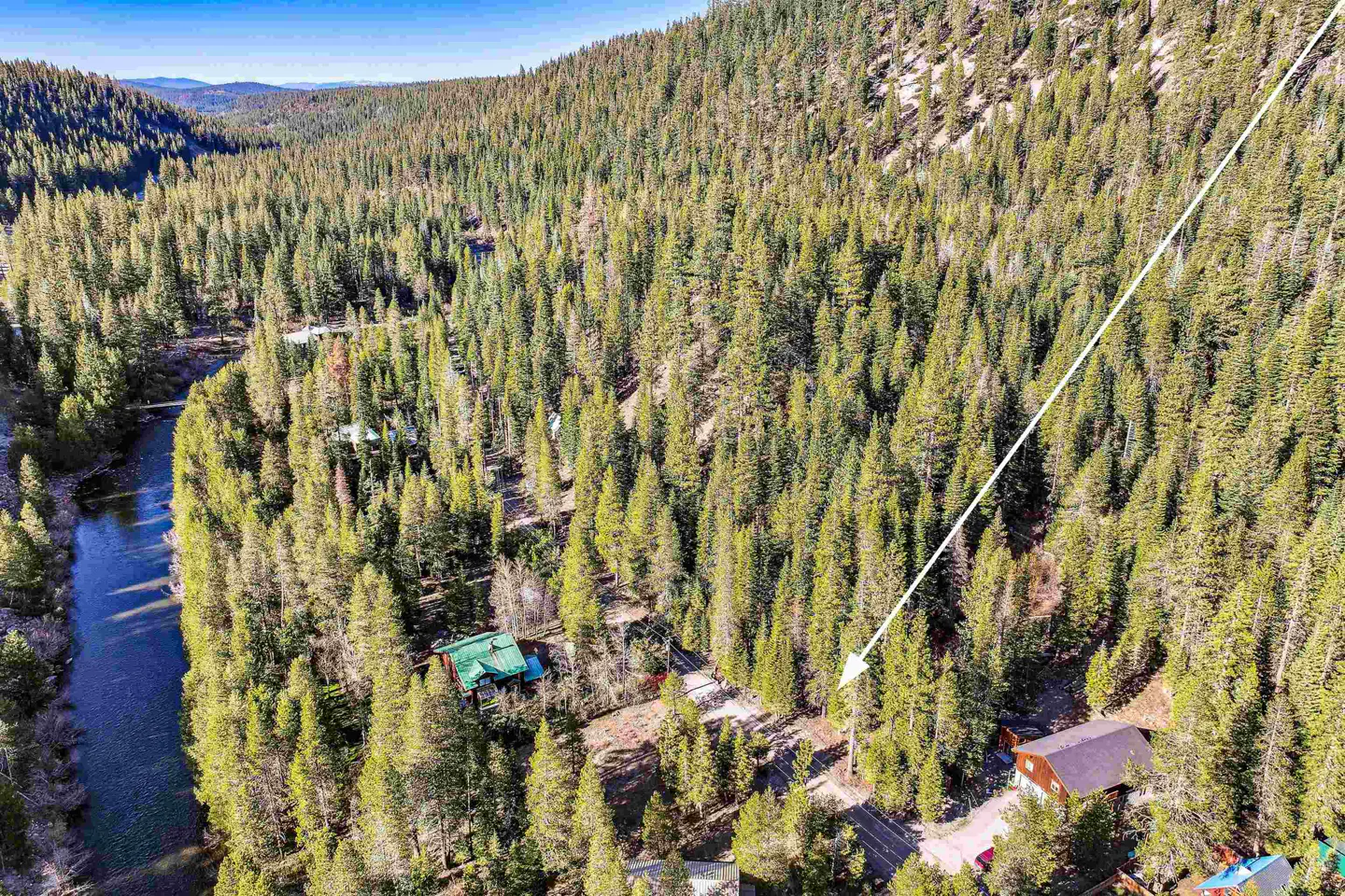 Aerial view of a wooded area with a river, houses, and an arrow pointing to a property.