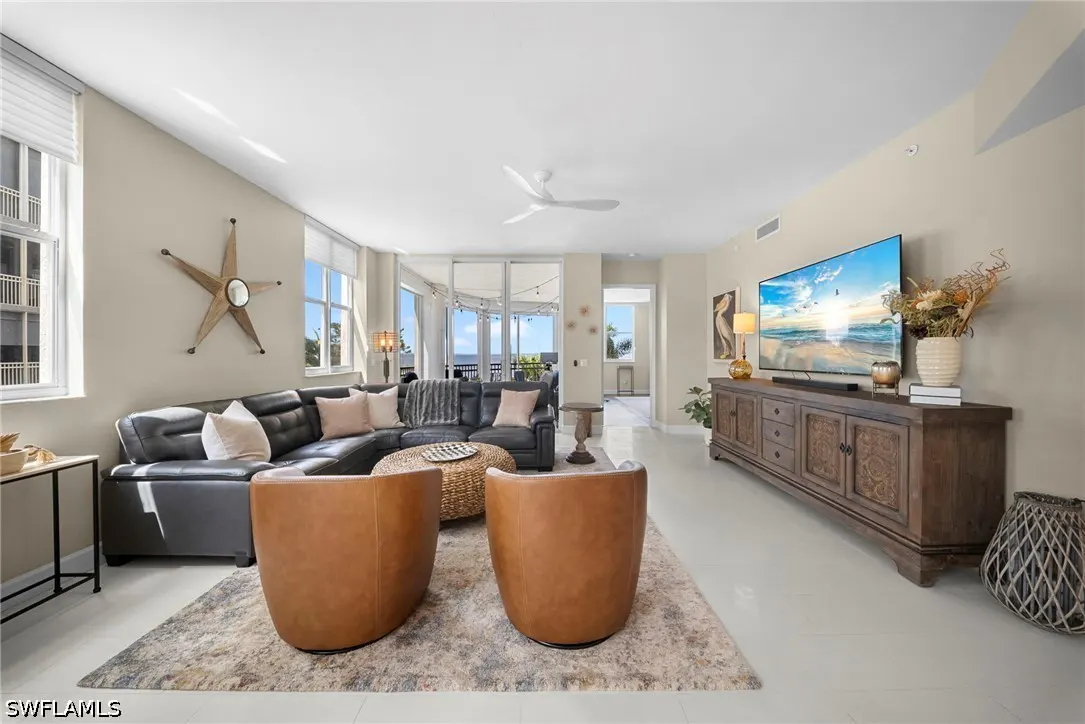 Living room with a black leather sectional, two brown chairs, a TV, and a view of the ocean.