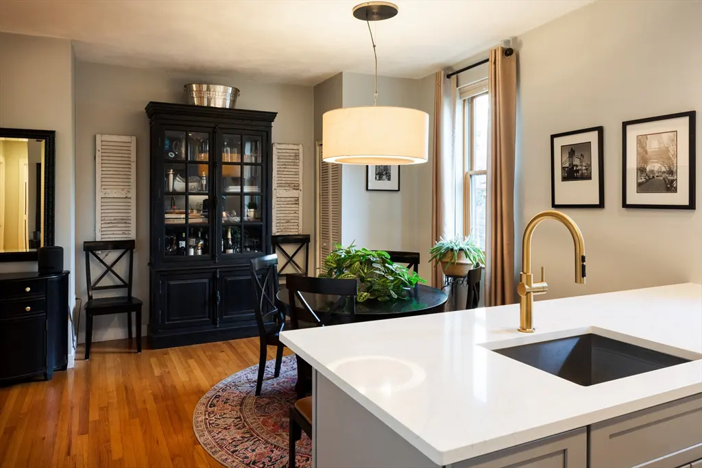 Modern kitchen with white island, gold faucet, and dining area featuring a black hutch, round table, and hardwood floors.