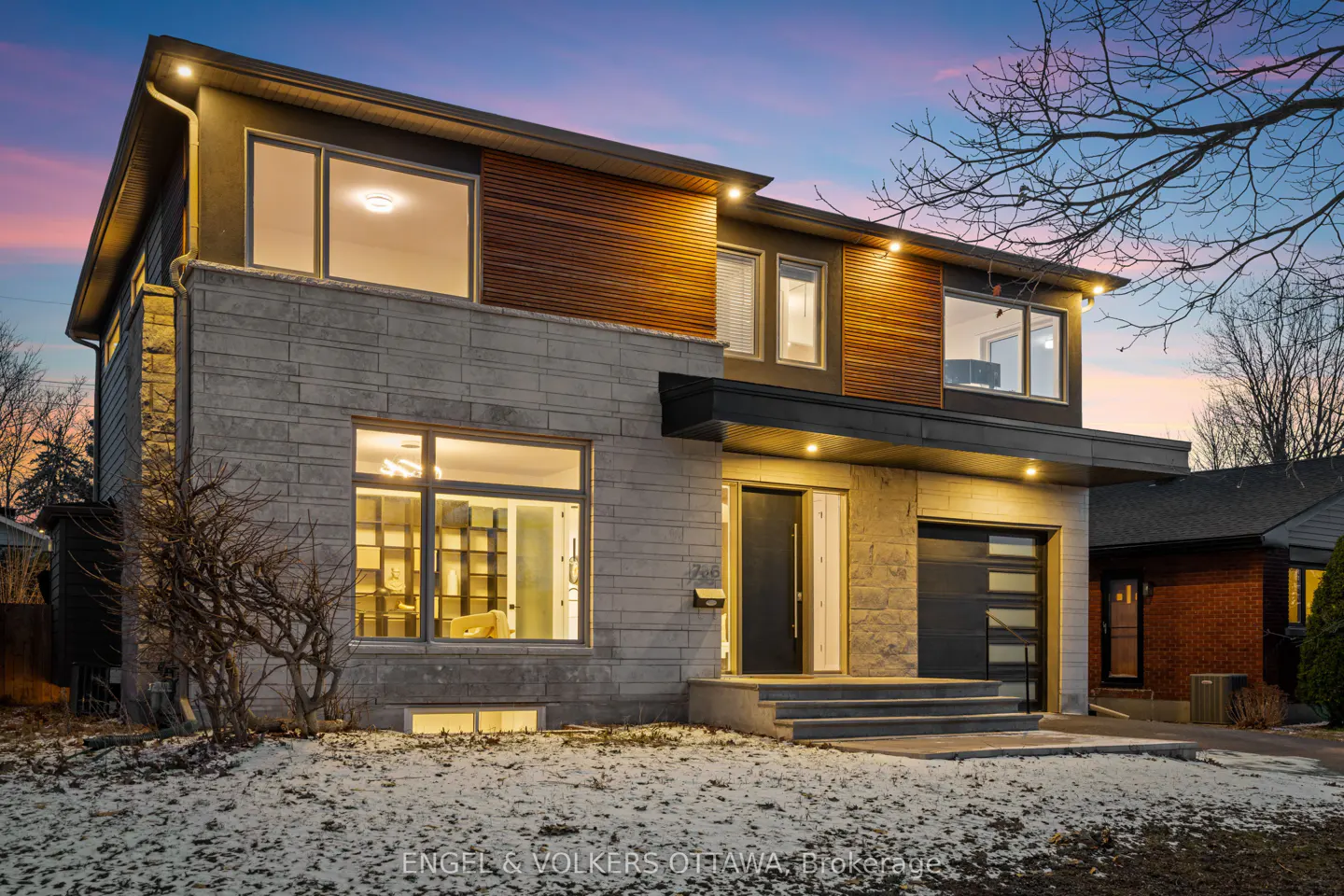 Two-story house with stone and wood exterior, large windows, and a black door and garage. The sky is a mix of pink and blue.