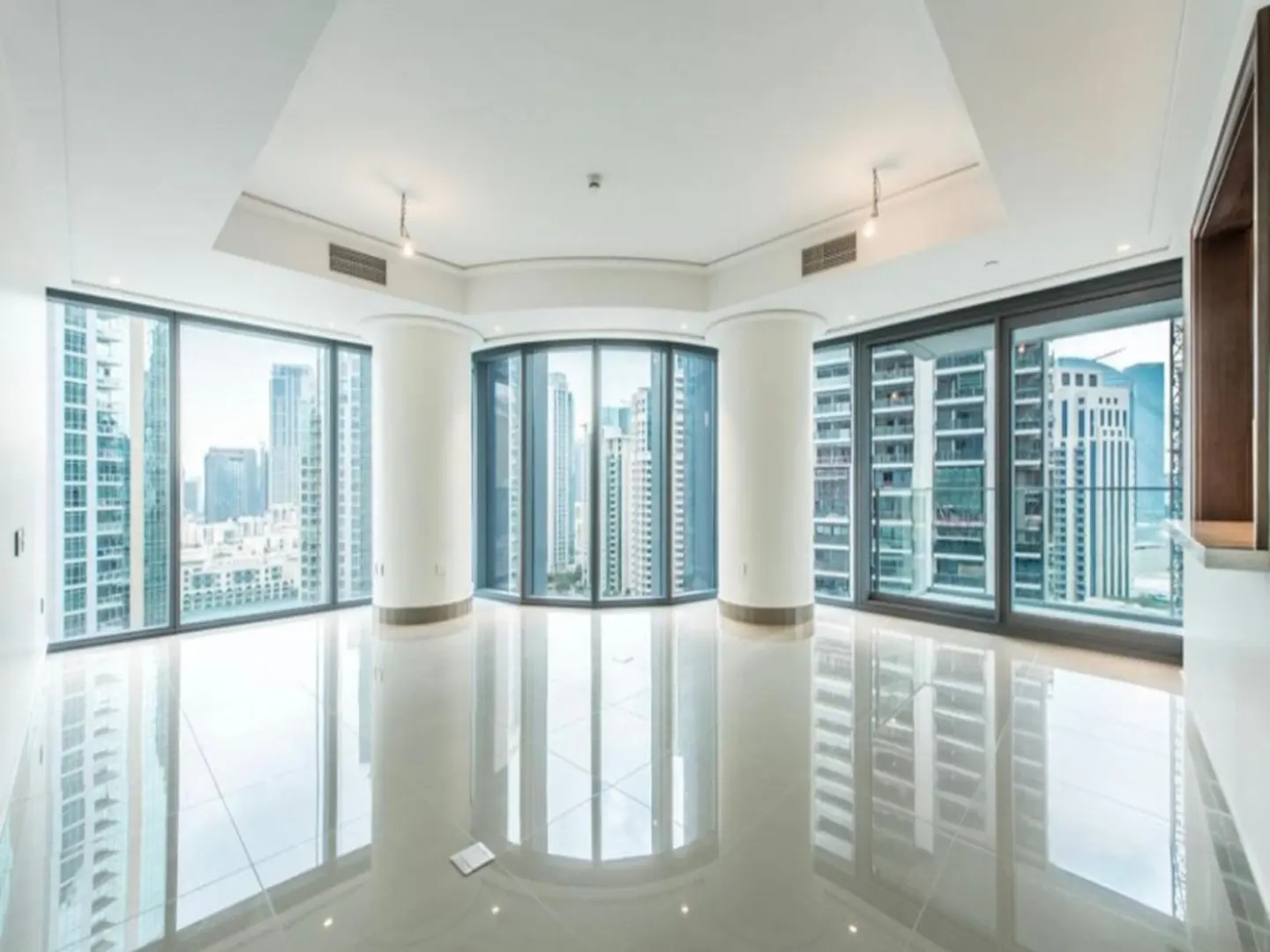 Bright, empty room with white tile floors, large windows, and white pillars. A city skyline is visible through the windows.