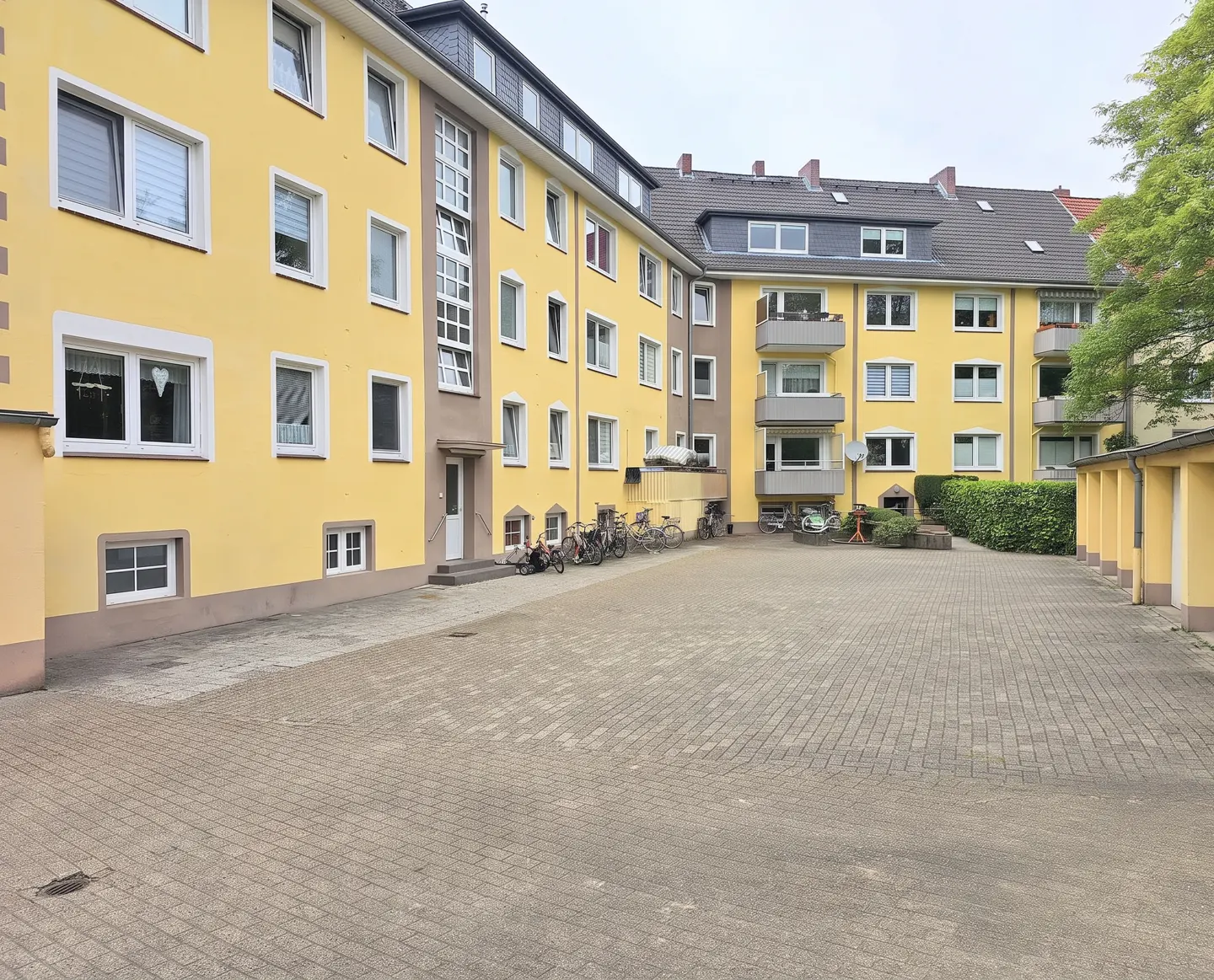 View of a yellow apartment building with a gray brick courtyard and parked bicycles.