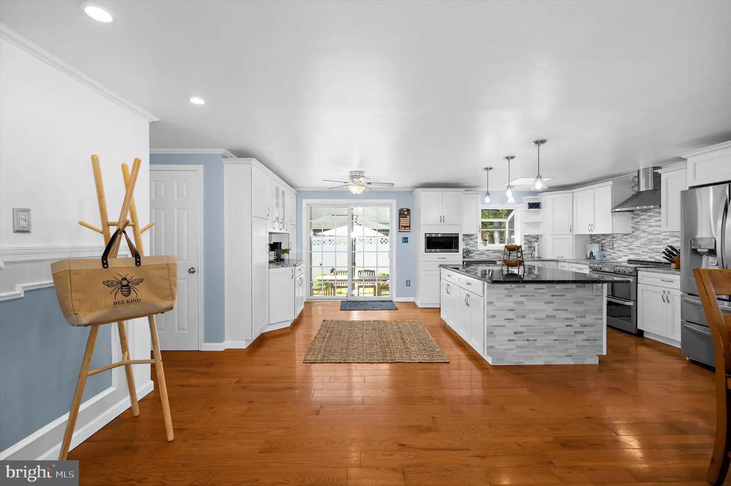 Bright, open kitchen with white cabinets, stainless steel appliances, and hardwood floors. A jute rug sits in front of sliding glass doors.