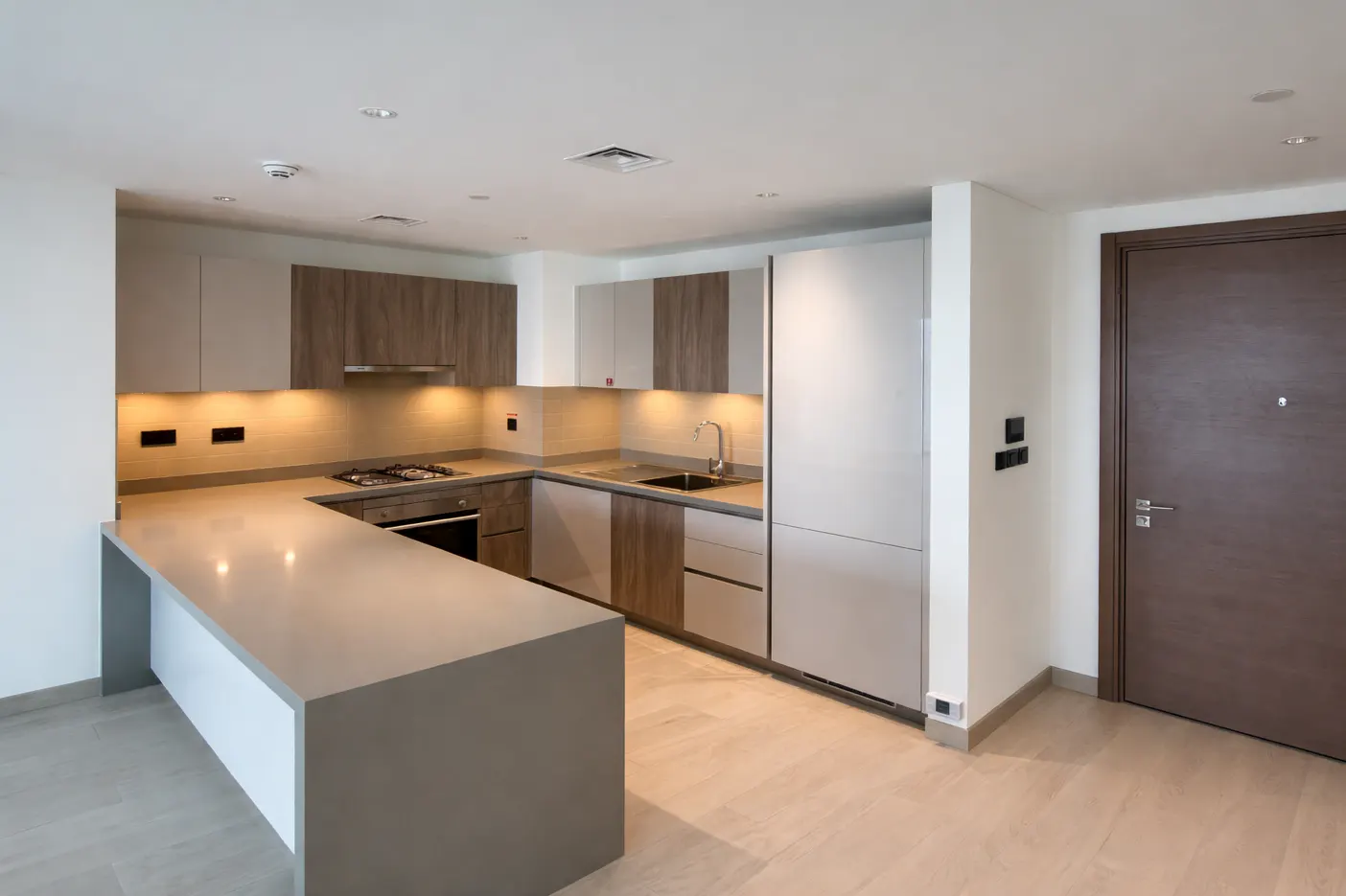 A modern kitchen with gray countertops, wood and white cabinets, and a brown door.