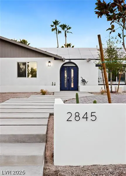 Modern white home with a blue arched front door, concrete walkway, and a wall displaying the address 2845.